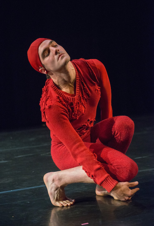 Silas Riener in a red knitted cap, tattered sweater and knit pants crouches near the ground